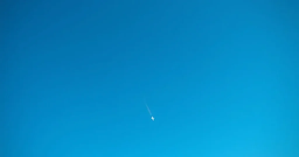 Airliner seen from below against a clear sky with a thin contrail