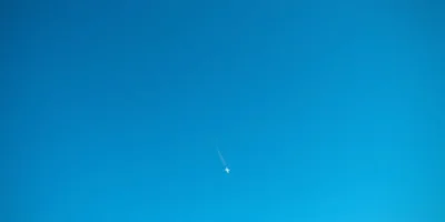 Airliner seen from below against a clear sky with a thin contrail