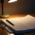 Desk with printed documents, a pen and reading glasses under a desk lamp